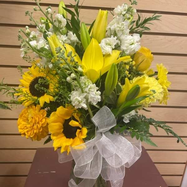Yellow lilies and sunflowers in a glass vase with a white ribbon