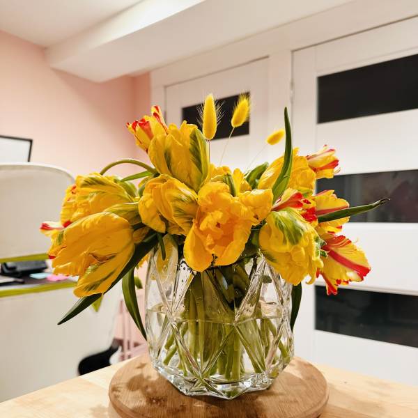 Yellow tulips in a clear glass vase on a wooden tray