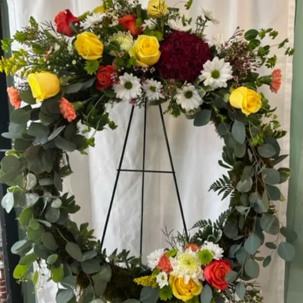 Large floral wreath with roses and daisies on a black stand