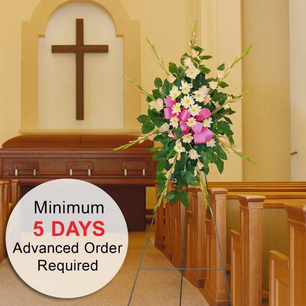 Standing spray of white and pink flowers with a pink bow on an easel in a church