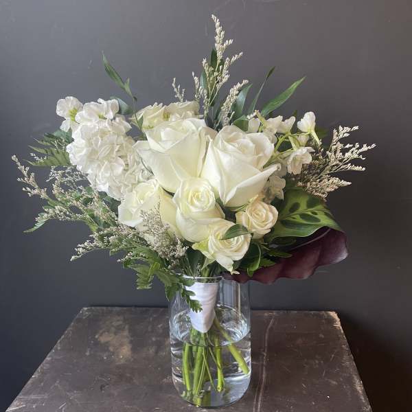 White rose bouquet in a clear glass vase with mixed greenery