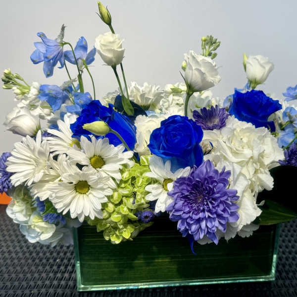 Blue, white, and purple flowers arranged in a rectangular glass vase