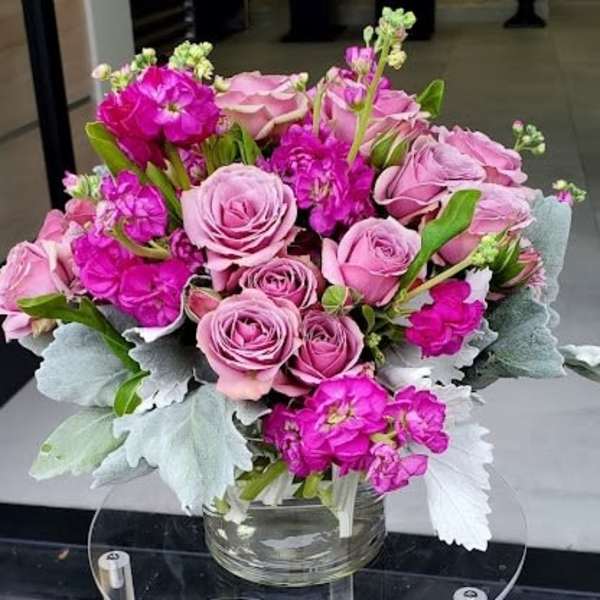 Compact arrangement of light pink roses and bright fuchsia blooms in a clear glass vase with silvery foliage