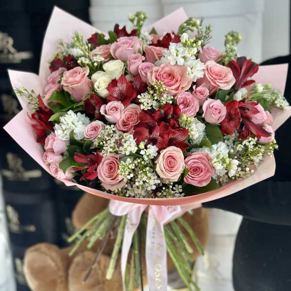 Bouquet of pink and red roses with white filler flowers wrapped in pink paper