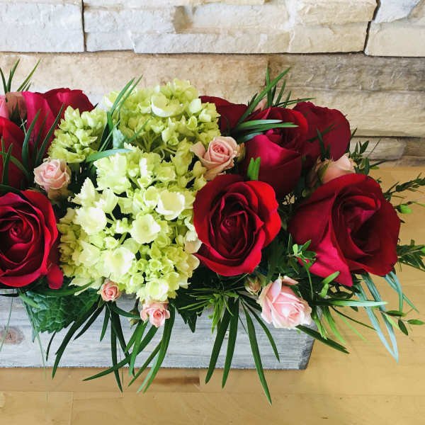 Red roses and pale green hydrangeas in a rectangular wooden box