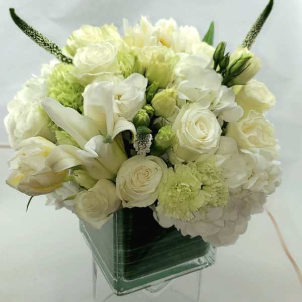 White and pale green bouquet in a clear square vase
