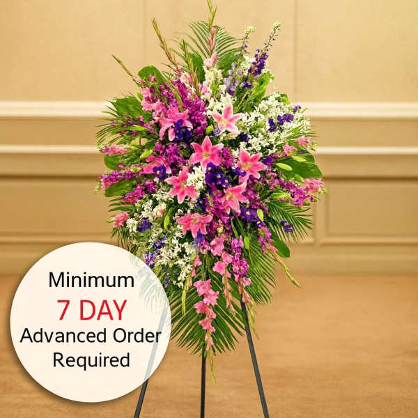 Tall standing spray with pink lilies and mixed purple and white flowers on a black easel stand