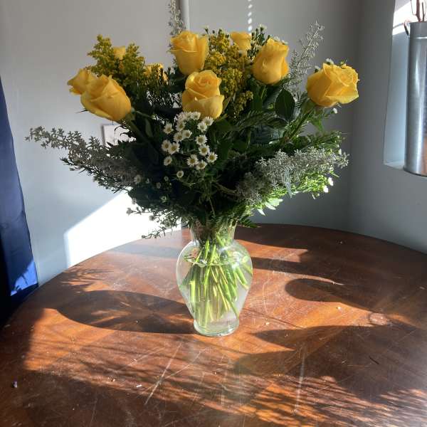 Yellow roses in a clear glass vase with small white filler flowers