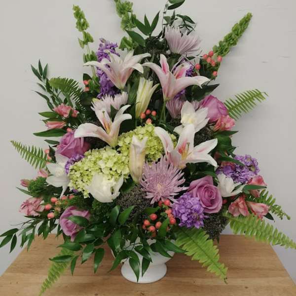 Large mixed floral arrangement in a white vase with lilies, roses, and purple blooms