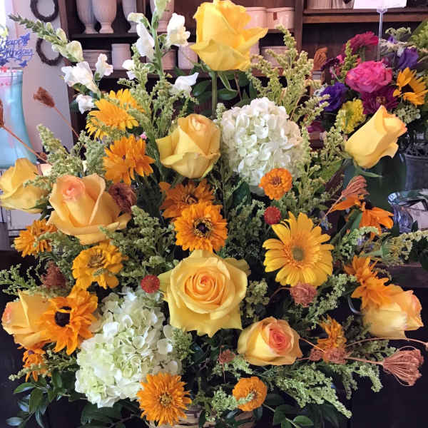 Basket arrangement of yellow roses, orange daisies, and white hydrangeas