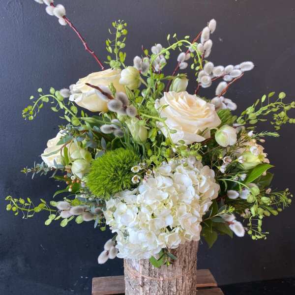 White roses and hydrangea in a rustic wood vase with green accents