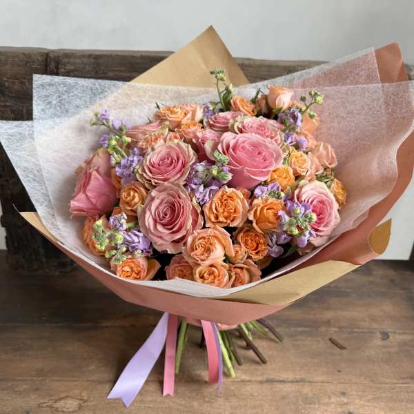 Bouquet of pink and peach roses with lavender accents in pastel wrap