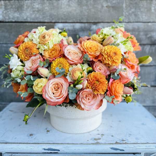 Peach and orange mixed flower arrangement in a white vase