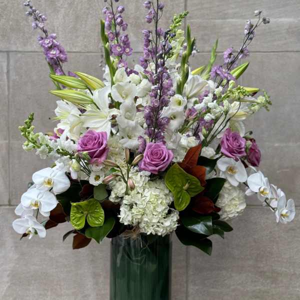 Tall bouquet of white orchids, lilies, hydrangeas, and purple roses in a glass vase