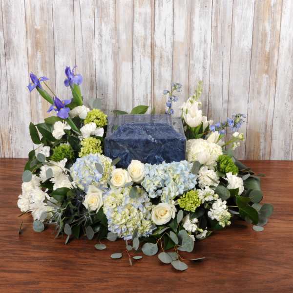 Low white and blue floral arrangement surrounding a square blue urn