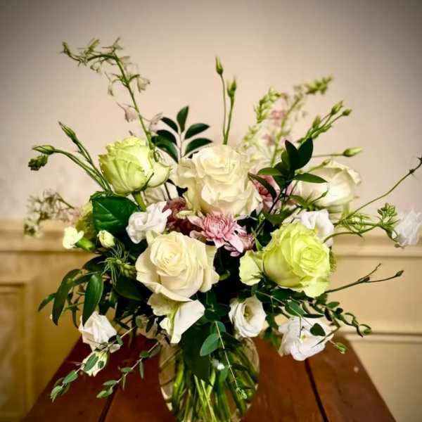 Arrangement of white and pale green roses with soft pink blooms in a clear glass vase on a wooden table