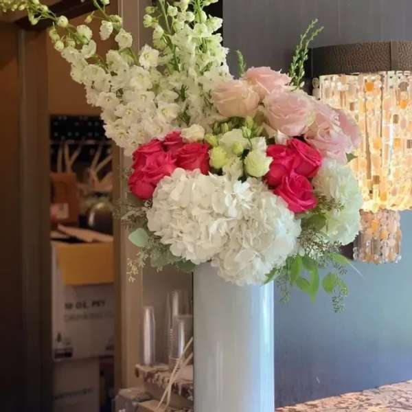 Tall floral arrangement with white hydrangeas, pink roses, and white blossoms in a white vase
