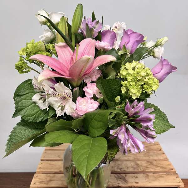 Pink lilies and purple flowers in a glass vase