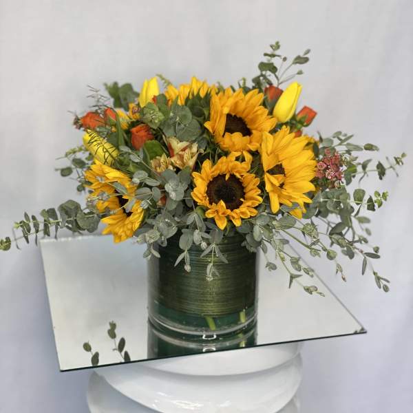 Sunflowers and orange roses in a green glass vase