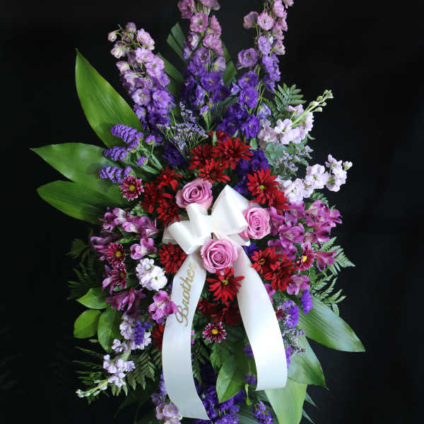 Tall standing floral spray with purple, pink, and red flowers and a white ribbon