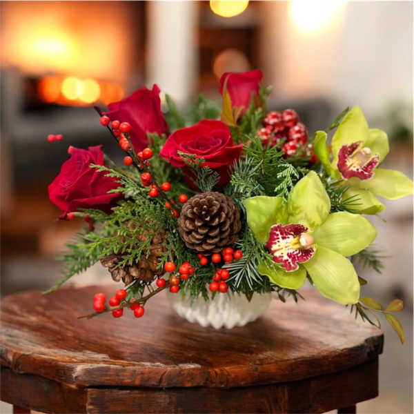 Holiday bouquet with red roses, green orchids, and pinecones in a white vase