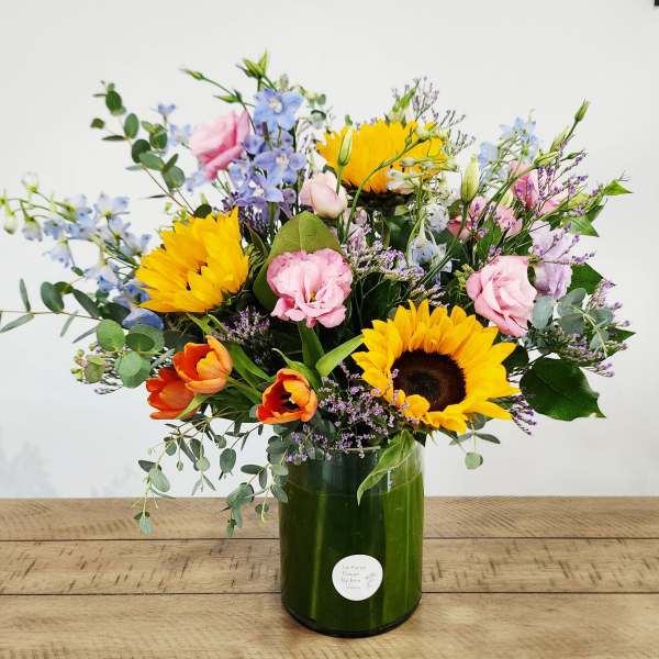 Mixed bouquet with sunflowers, pink blooms, and blue flowers in a green vase