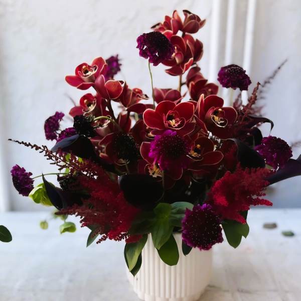 Deep red orchid arrangement in a white vase with dark purple accents