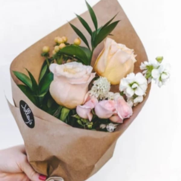 Hand-tied bouquet of pale roses and white flowers in brown paper