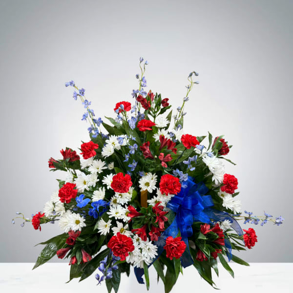 Red carnations and white daisies with blue flowers in a ribboned arrangement