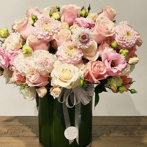 Pink and cream rose bouquet in a dark green vase with a sheer ribbon