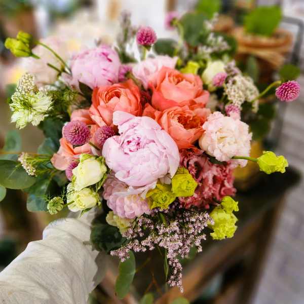 Handheld bouquet of pink and peach flowers with small accent blooms