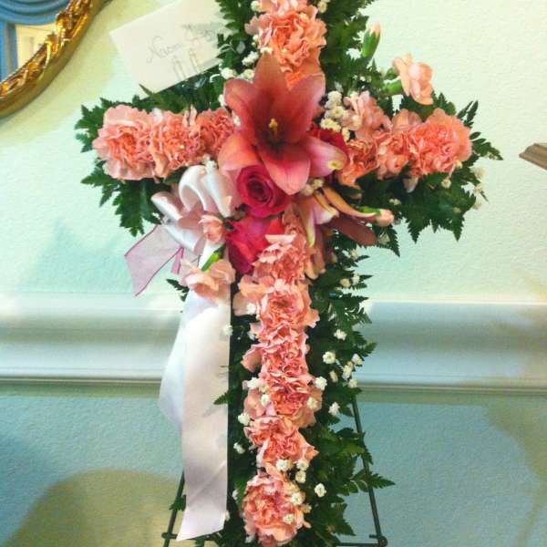 Cross-shaped floral funeral spray with pink carnations and lilies
