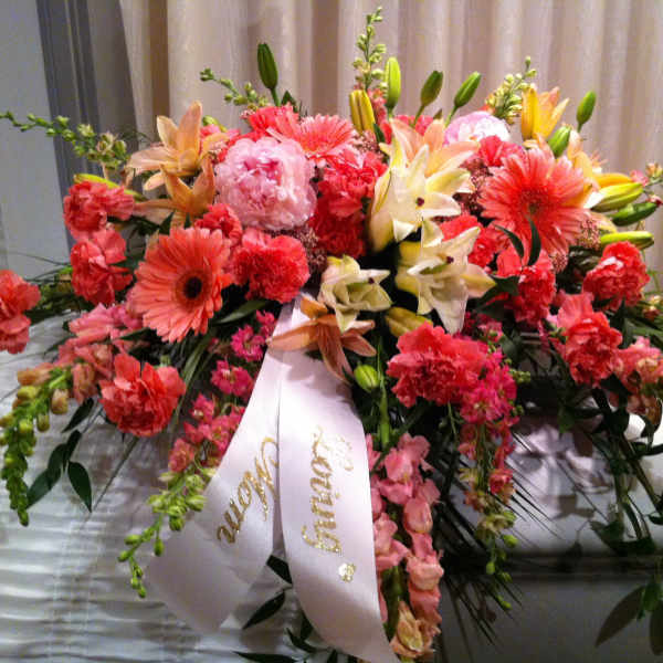 Large pink and coral floral spray with a white ribbon draped over a casket