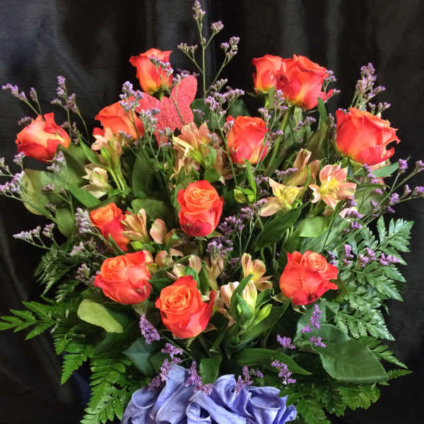 Orange roses and alstroemeria in a glass vase with a purple ribbon