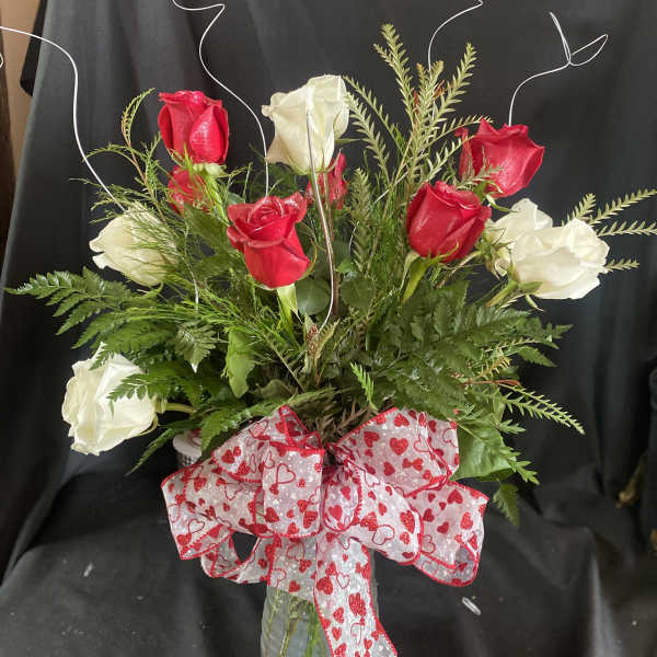 Red and white roses in a glass vase with a heart-patterned bow