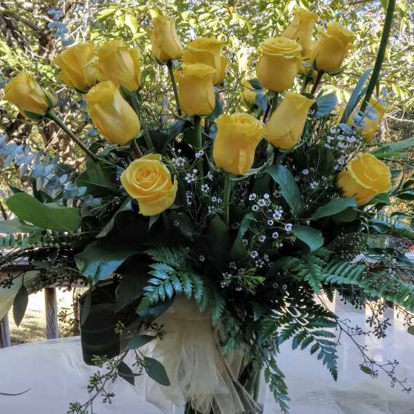 Yellow roses arranged in a clear glass vase with greenery
