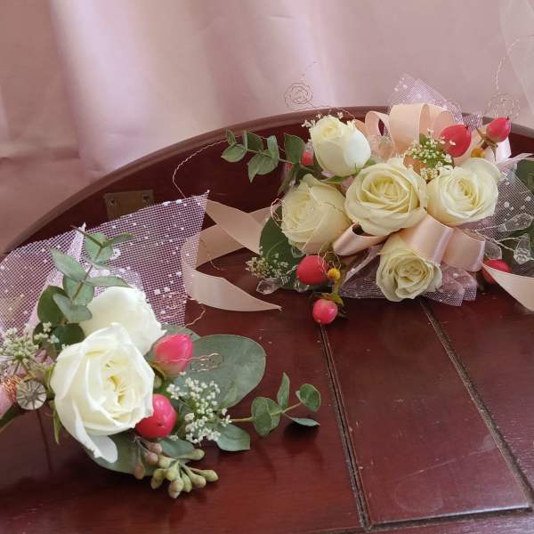 Two small rose bouquets with pink ribbon and greenery on a wooden bench