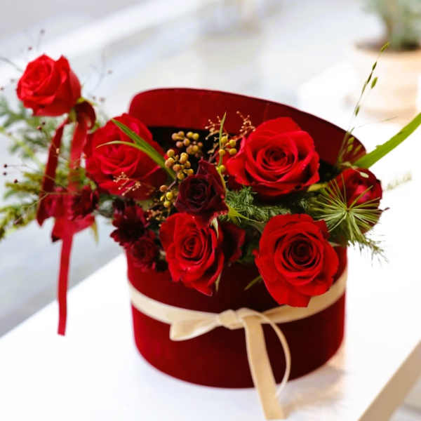 Red roses arranged in a burgundy hat box with a cream ribbon