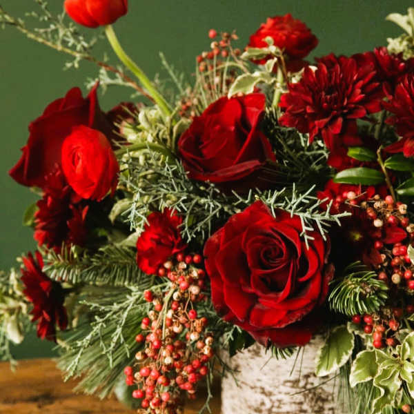Red roses and red blooms in a white vase with berries and greenery