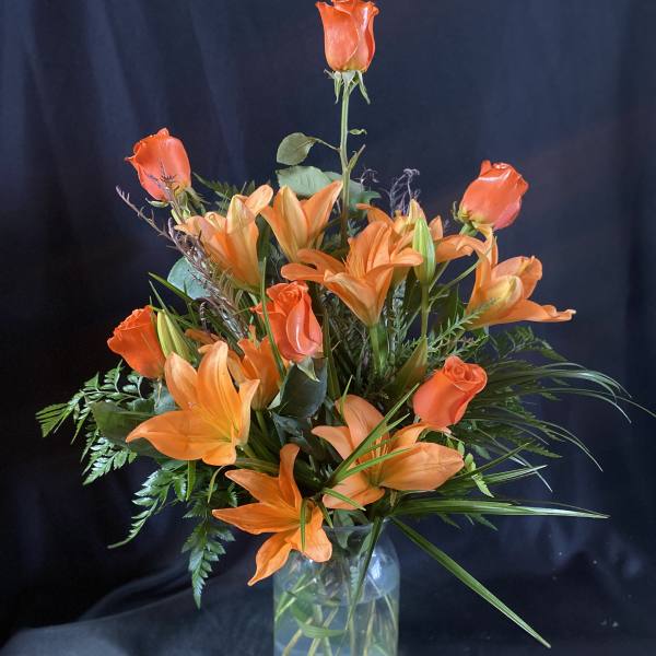 Orange roses and lilies arranged in a clear glass vase