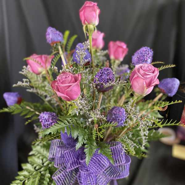 Pink roses and purple flowers in a glass vase with a purple ribbon