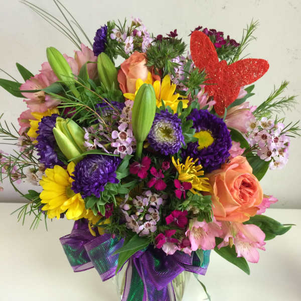 Colorful mixed bouquet in a clear glass vase with a red butterfly pick