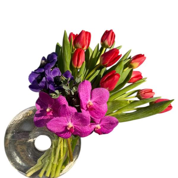 Bouquet of red tulips and purple orchids in a round glass vase