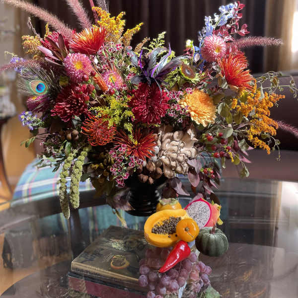 Colorful mixed floral arrangement with fruit accents in a dark vase