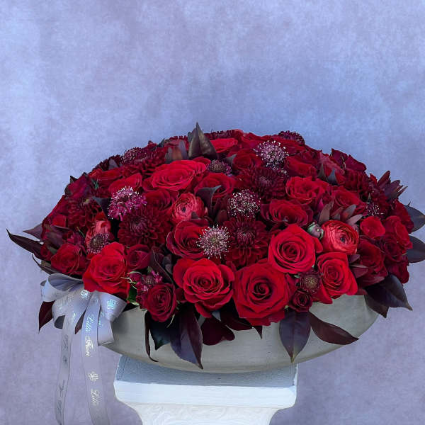 Large red rose arrangement in a shallow white container with a ribbon