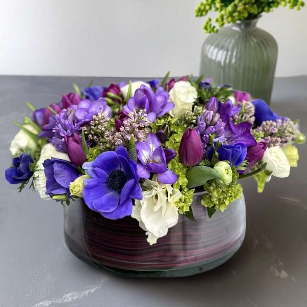 Purple and white flower arrangement in a low glass vase