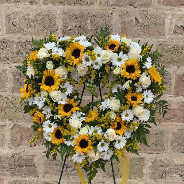 Heart-shaped floral wreath with sunflowers, white roses, and daisies on a stand