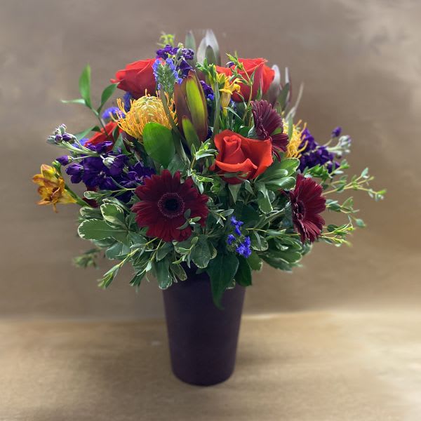 Mixed bouquet of red roses, burgundy daisies, and purple flowers in a dark vase