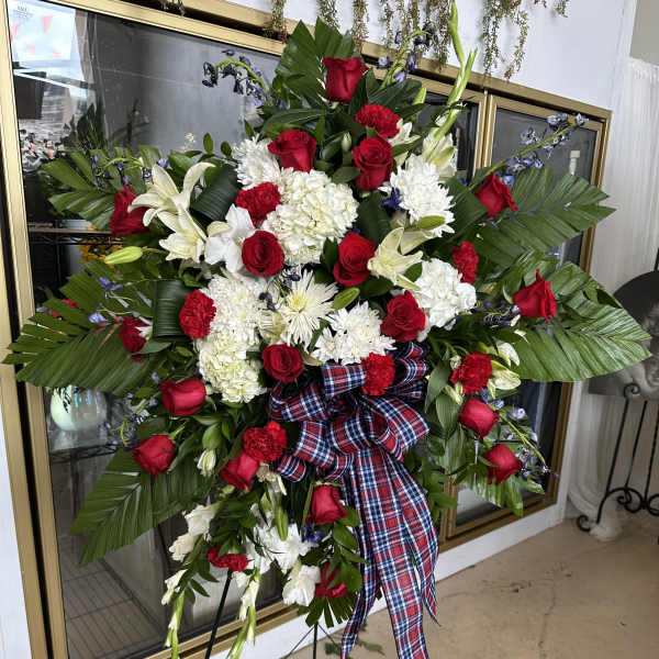 Standing floral spray with red roses, white lilies, and a plaid ribbon