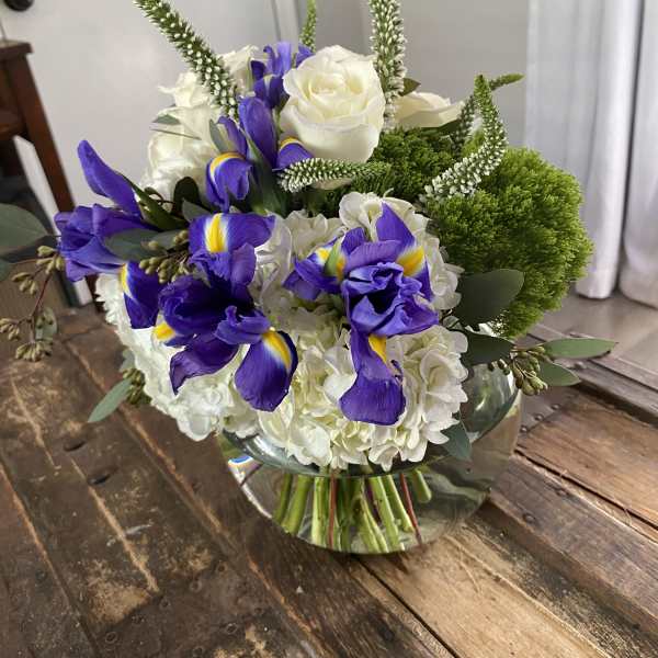 Bouquet of white roses, purple irises, and green accents in a glass vase
